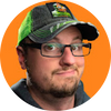 A man wearing a green and black baseball cap with a graphic logo on the front.